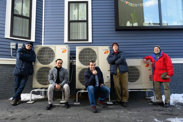 A modeling study by an MIT team has shown that electrifying residential heating can be a substantial step toward reducing carbon emissions, as well as costs, over the combined electricity and natural gas sectors. Here, the team poses beside a high-efficiency electric heat pump system that provides heating to the home, replacing the natural gas-fired furnace. Left to right: Audun Botterud, Saurabh Amin, Rahman Khorramfar, Morgan Santoni-Colvin, and Leslie Norford. Not pictured: Dharik Mallapragada.